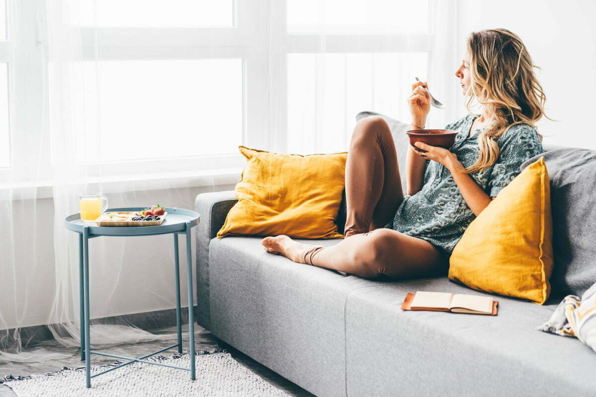 Woman eating on the couch while recovering from a plastic surgery procedure