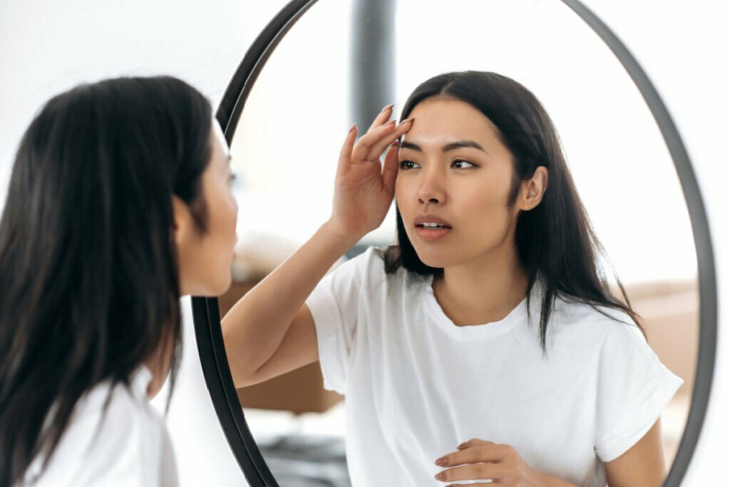 Young woman looking at skin in the mirror after non-surgical treatments at a med spa to treat acne