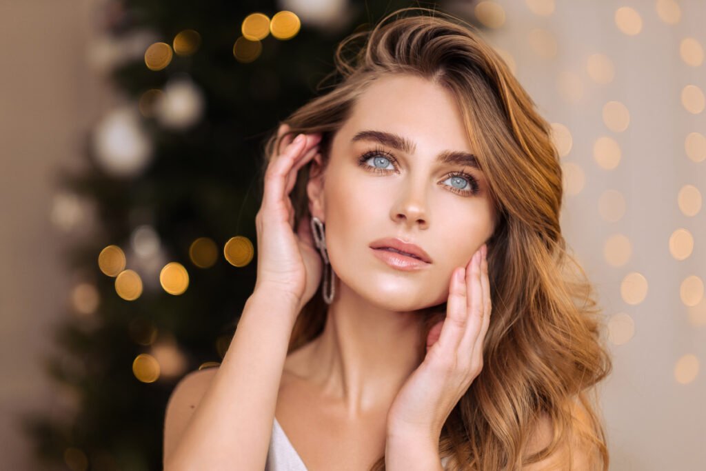 Beautiful woman touching face with glowing skin in front of holiday lights