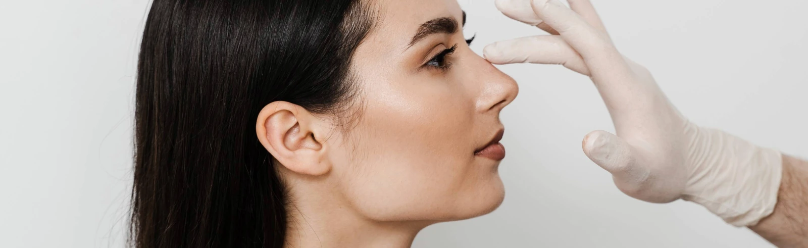 plastic surgeon examining young woman's nose during rhinoplasty consultation