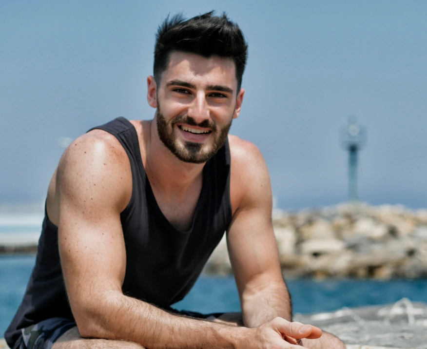 Happy man sitting by the shoreline wearing tank top