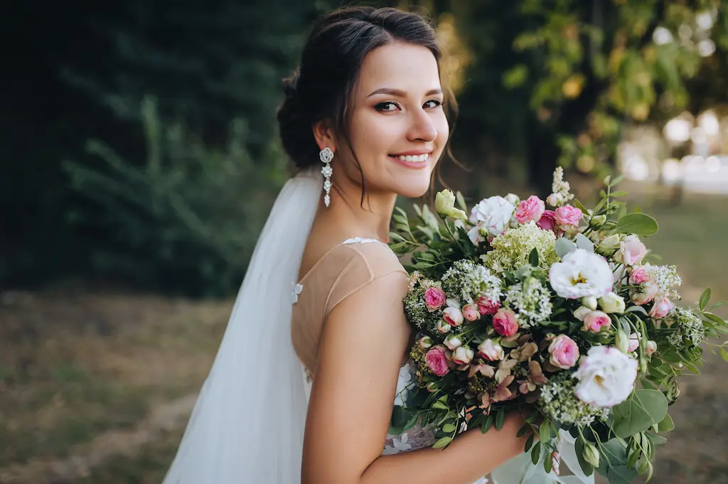 A beautiful bride stands on nature in greenery with a large bouquet. Wedding portrait close-up of the young bride.